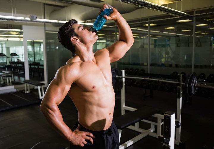 Shirtless muscular man drinking energy drink in gym